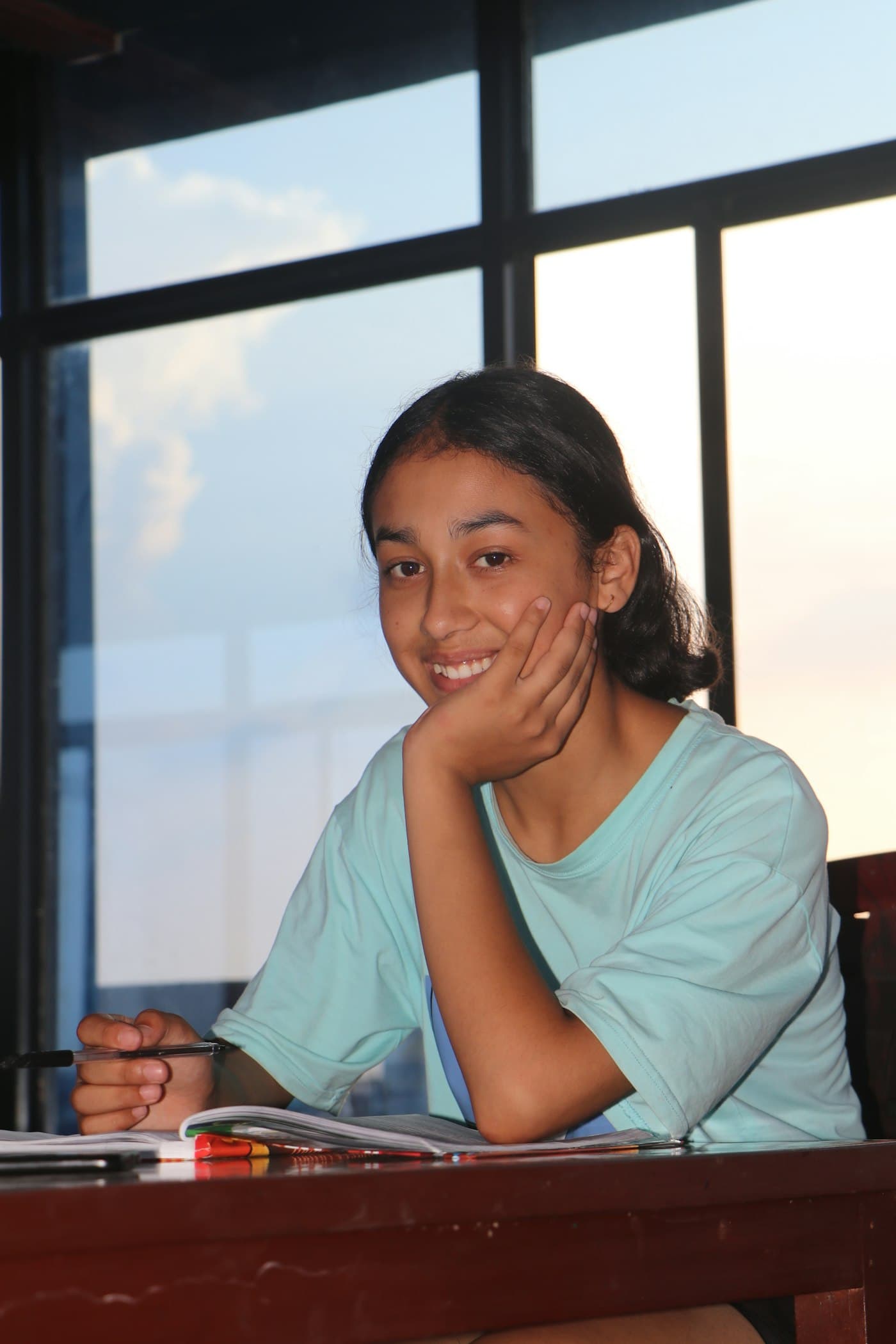 A high school student smiling at her desk with a pen and an open notebook